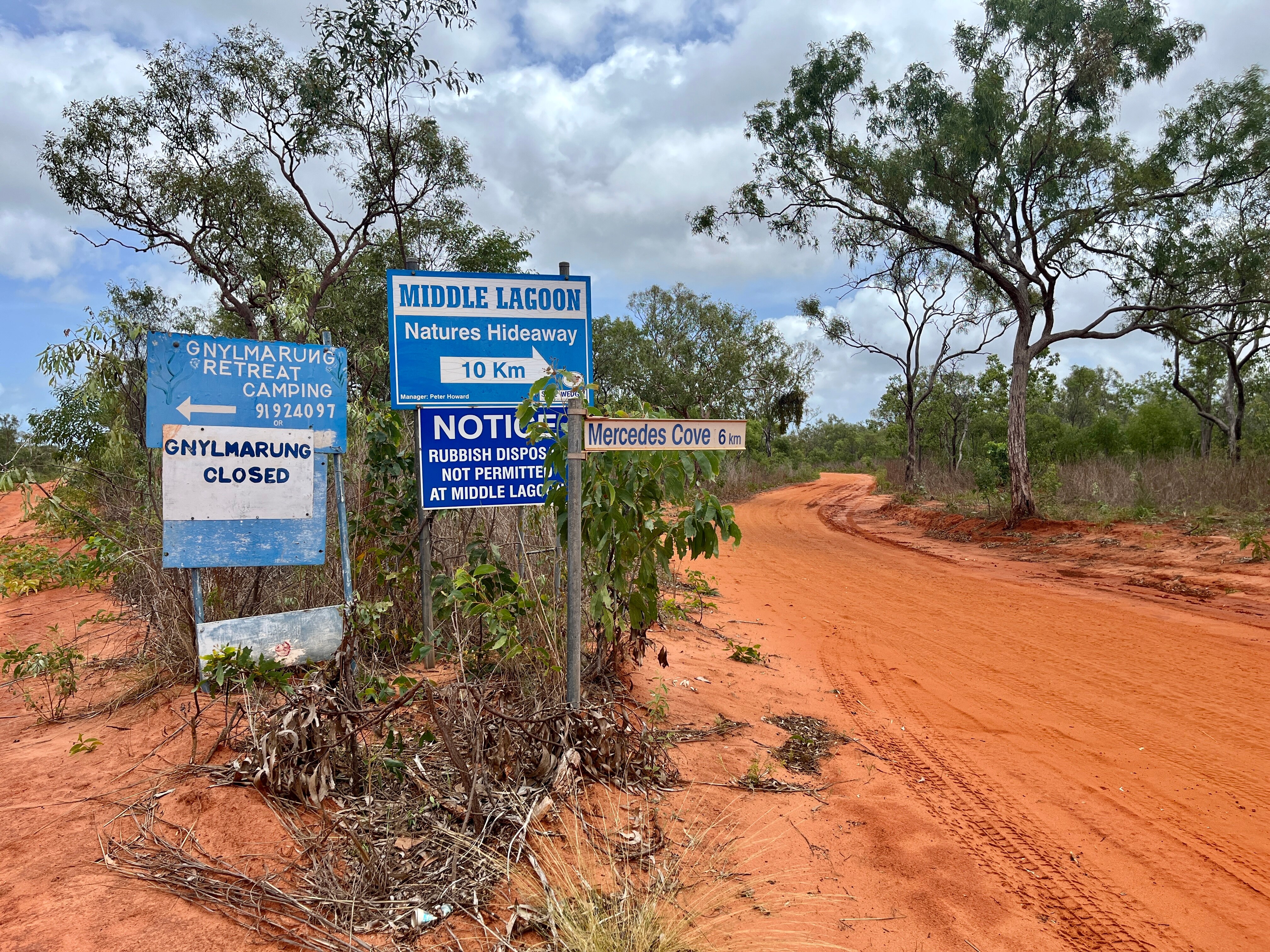Blue signs pointing to camps next to a red desert track.