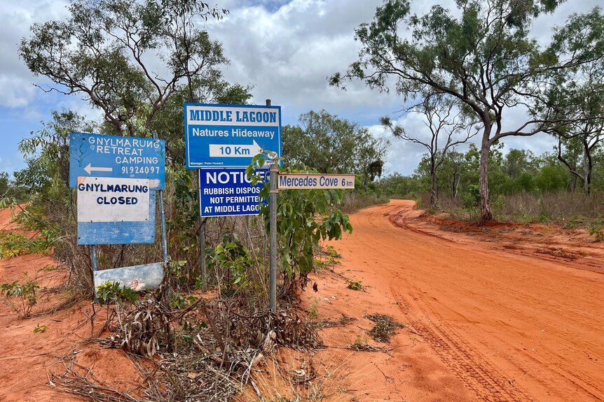Blue signs pointing to camps next to a red desert track.