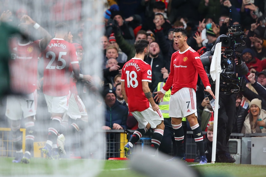Un futbolista estrella se para, con la boca abierta, en el banderín de esquina mientras sus compañeros de equipo corren hacia él después de su gol en la Premier League.