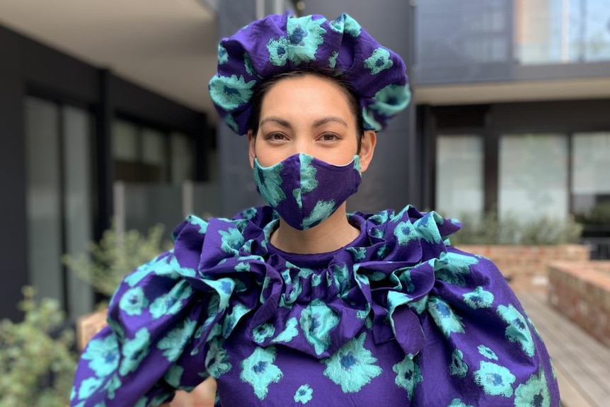 A woman in a blue and purple dress with matching face mask and hat.