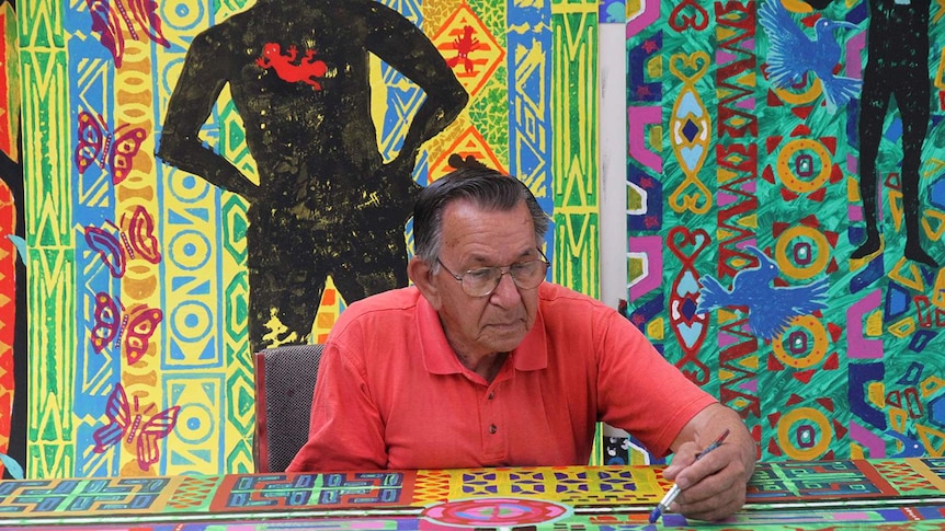 Ted Laxton surrounded by brightly coloured large scale artwork, working on another painting in front of him.