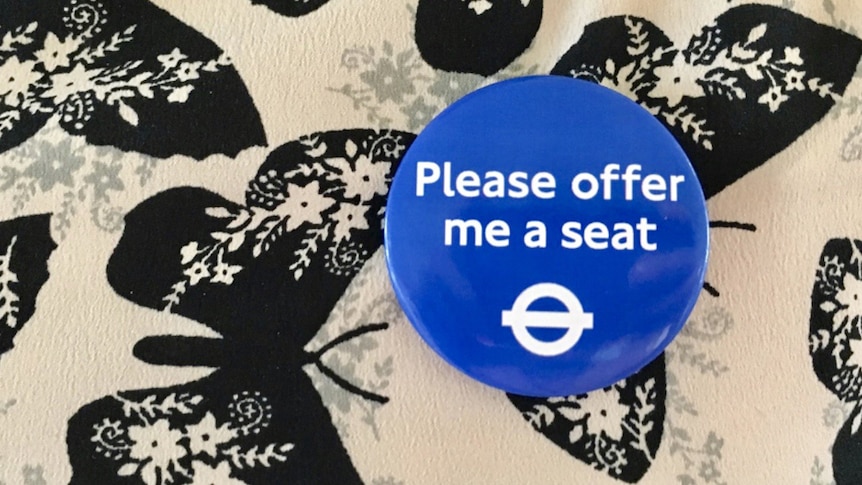 A commuter wears a blue badge that says 'Please offer me a seat'.