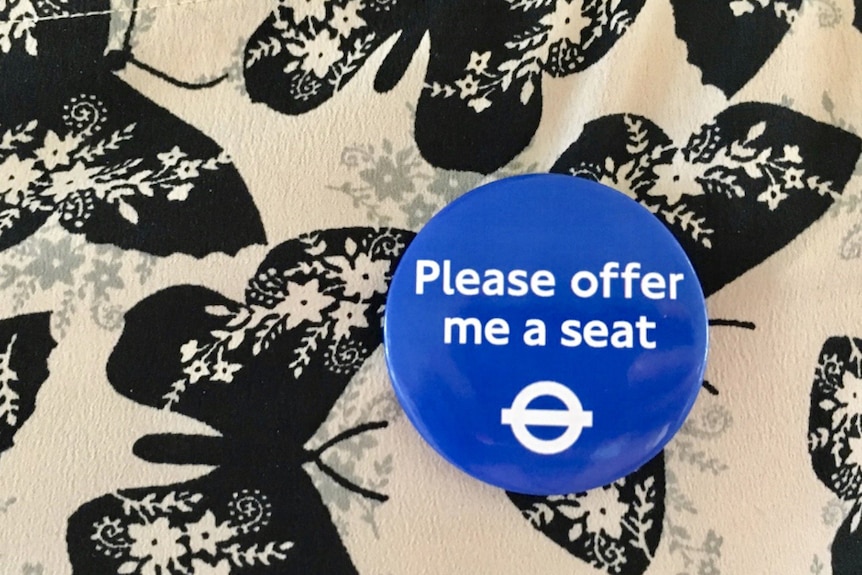 A commuter wears a blue badge that says 'Please offer me a seat'.