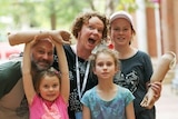 Mandy and husband and daughters smiling at camera while holding up her prosthetic arms.