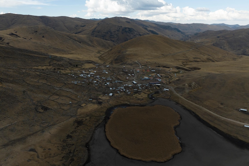 An aerial photo of a dark green brown valley, where a small town sits next to a dried up lake bed. 