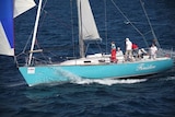 Crew members stand on board Finistere as it sails on the ocean.