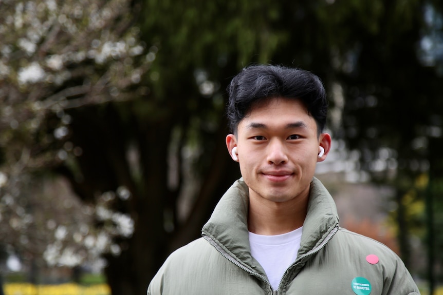 A man wearing a green jacket and white tshirt looking directly ahead.