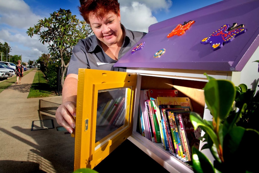 Librarian holds open the door to a cabinet full of books installed outside a child care centre.