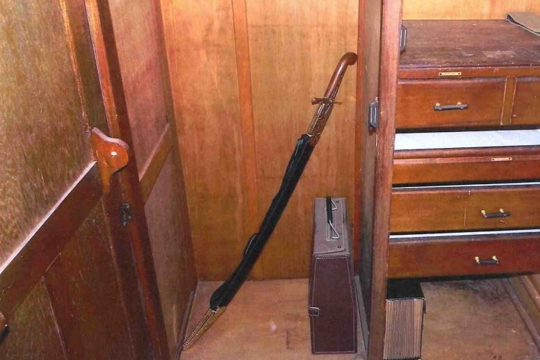 A long, sheathed sword in a wooden cabinet.