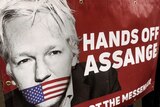 Protesters hold a banner saying Hands off Assange next to a picture of Julian Assange.
