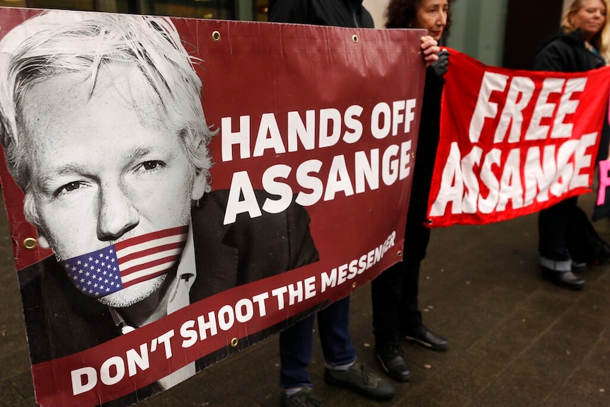 Protesters hold a banner saying Hands off Assange next to a picture of Julian Assange.