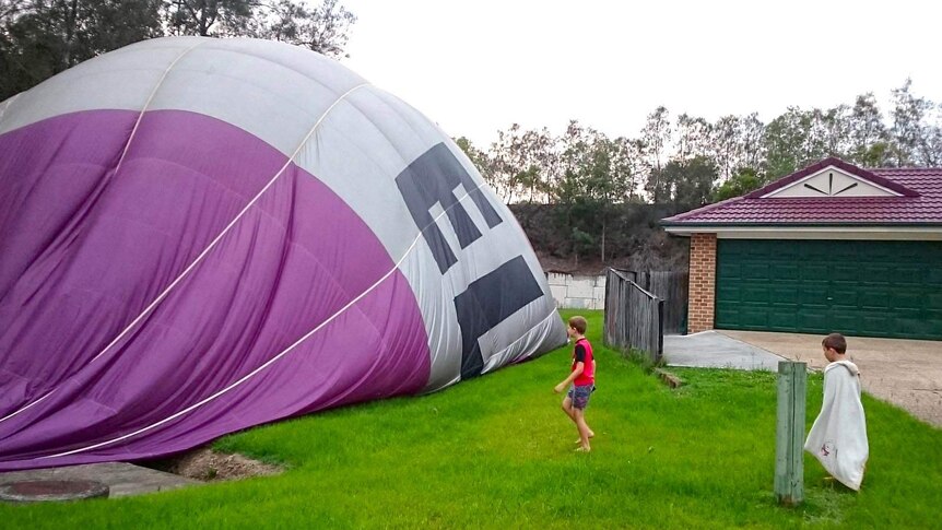 Two boys look at the half deflated hot air balloon in the backyard of the house.