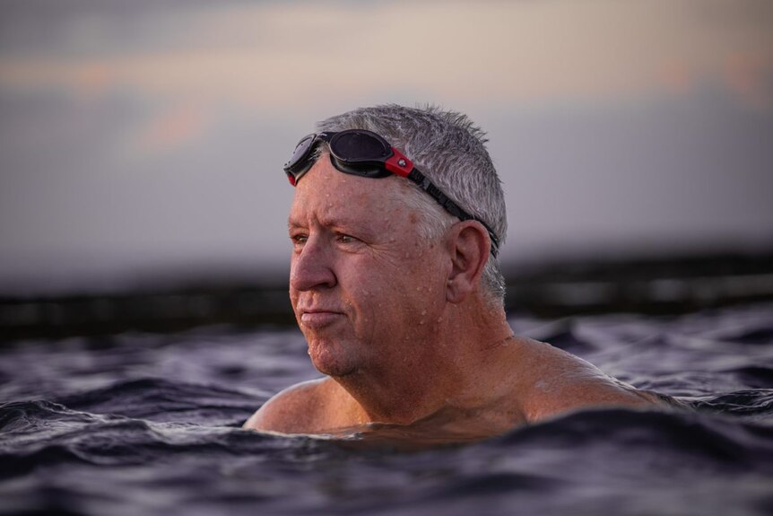 Paul Smith in the ocean with goggles on his head at sunrise