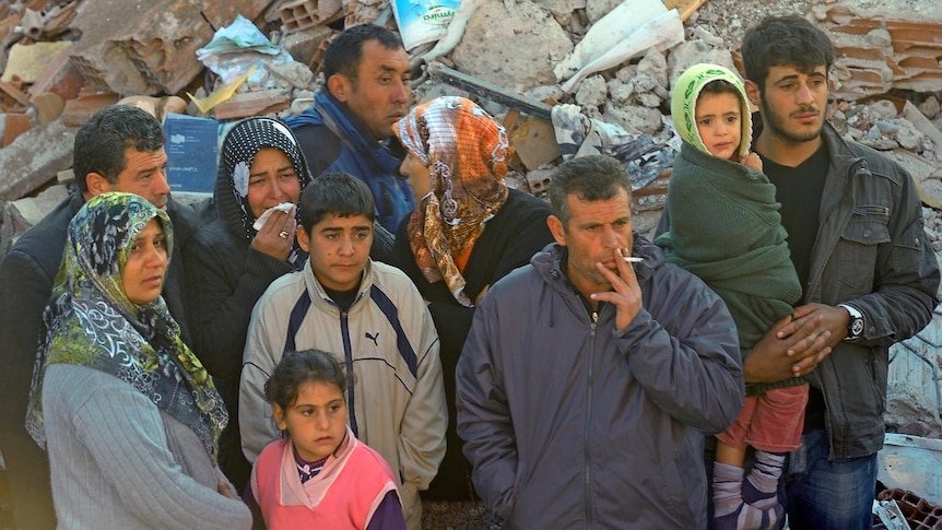 Relatives of victims stand next to the rubble of a damaged house after an earthquake in the Ercis province of Van