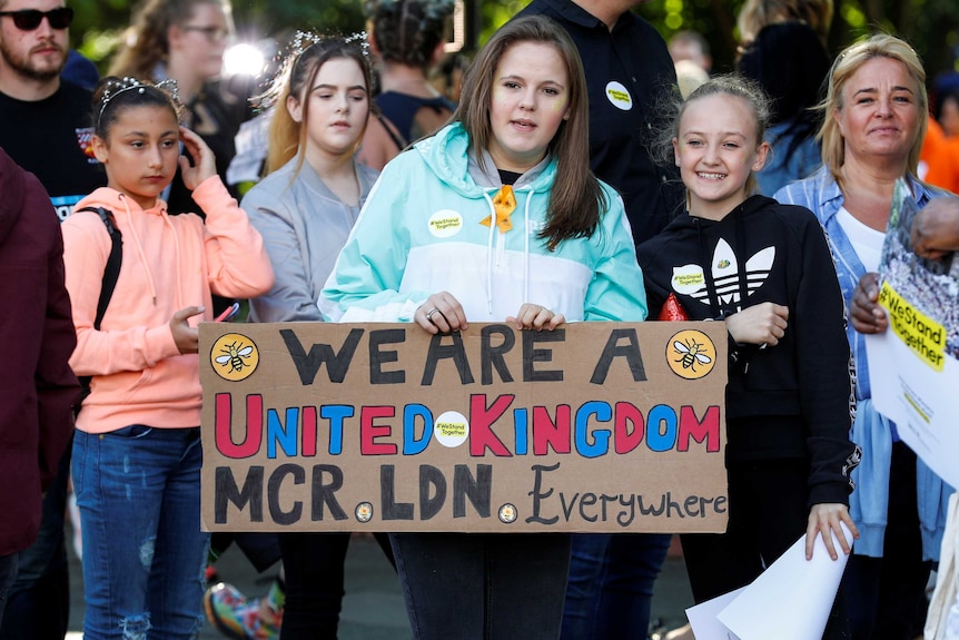 Four girls hold a banner decorated with bees and a message that reads: "We are a United Kingdom.MCR. LDN. Everywhere."