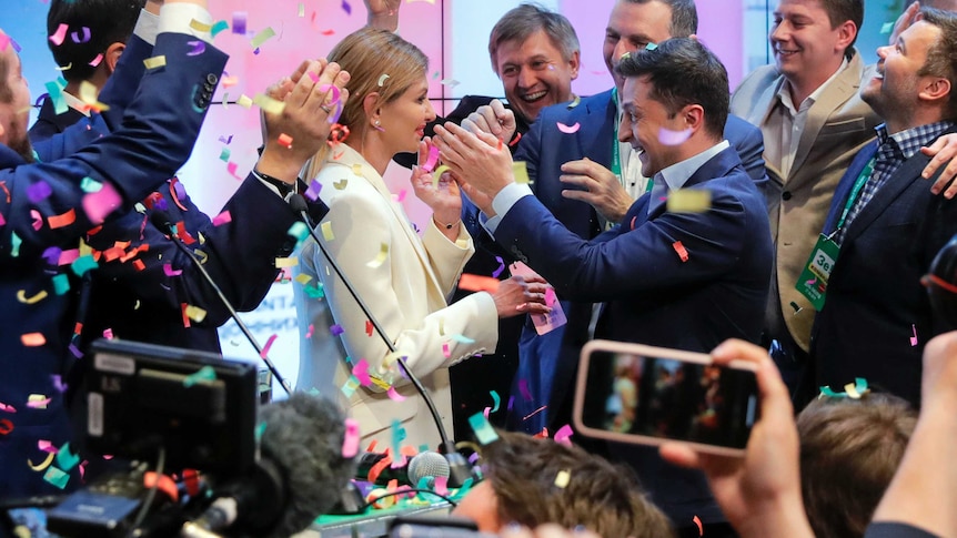 Volodymyr Zelenskiy embraces his wife Olana Zelenska, surrounded by supporters who are cheering on him.