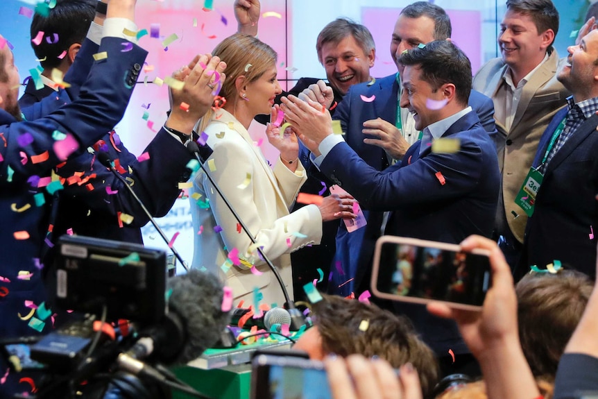 Volodymyr Zelenskiy embraces his wife Olana Zelenska, surrounded by supporters who are cheering on him.