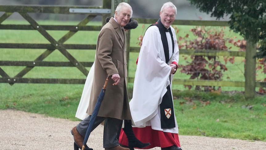King Charles walks alongside a clergyman in formal wear 