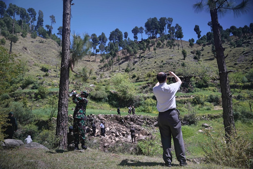 People taking photos around a rocky crater in a forest clearing.
