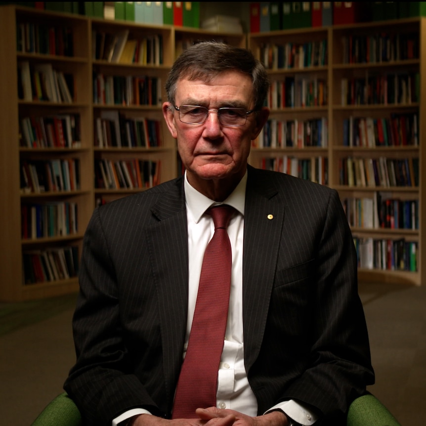 Dressed in a suit and tie, Angus Houston sits in a chair in an office, looking into camera with a serious expression.