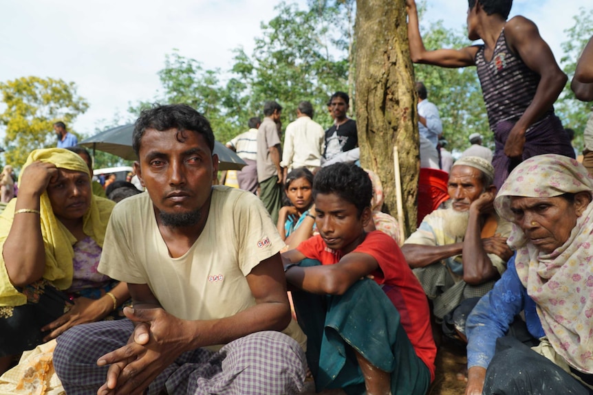 A male refugee crouches in front of the camera surrounded by family members.