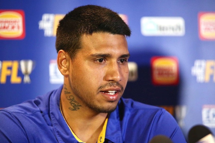 A head and shoulders shot of Tim Kelly wearing a blue West Coast Eagles shirt speaking at a media conference.