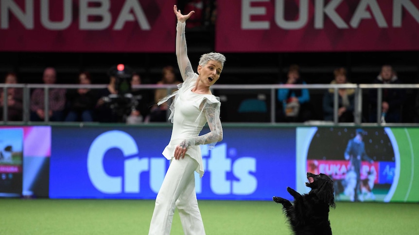 A woman in a white costume poses dramatically next to her dog standing on its hind legs.