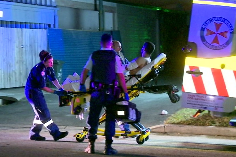 Three ambulance officers outside an ambulance with a man on an ambulance trolley.