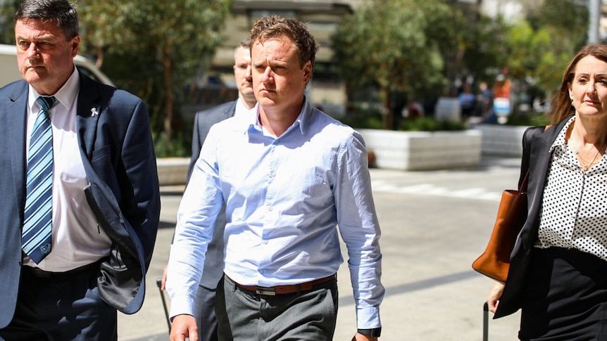 Brent Wyndham in a pale shirt, walking with lawyers.