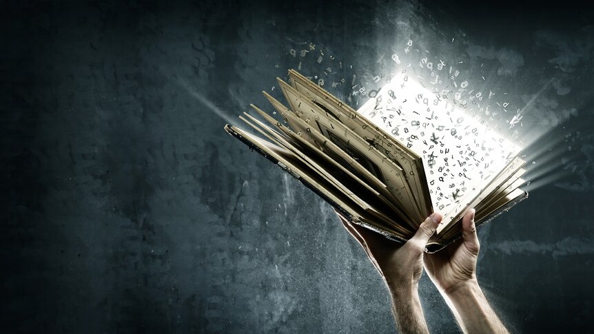 Two hands holding a book with a strong light and floating alphabet letters emanating from the centre