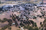 Aerial view of town flooded. Roofs and trees are visible above the brown sea of water.