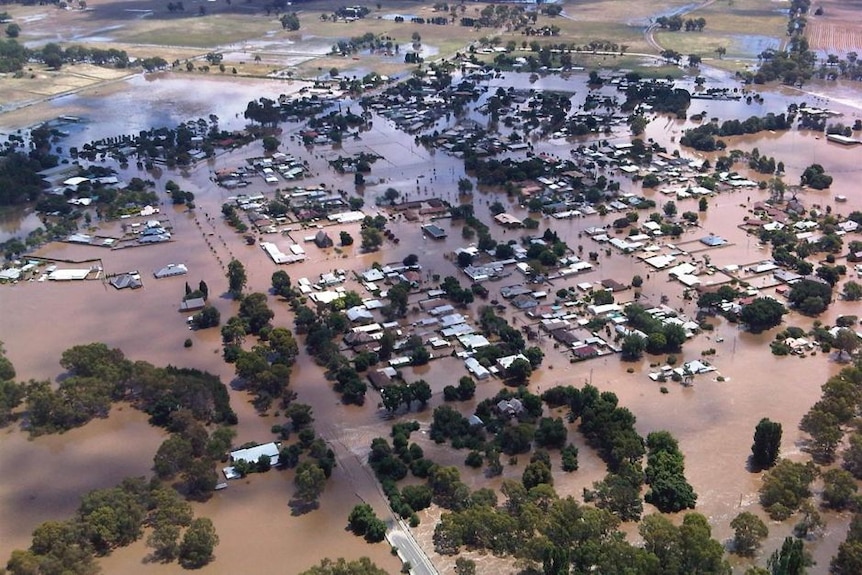 Aerial view of town flooded. Roofs and trees are visible above the brown sea of water.