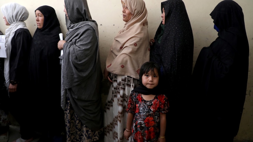 A girl looks at the camera next to a  line of women in head scarves 