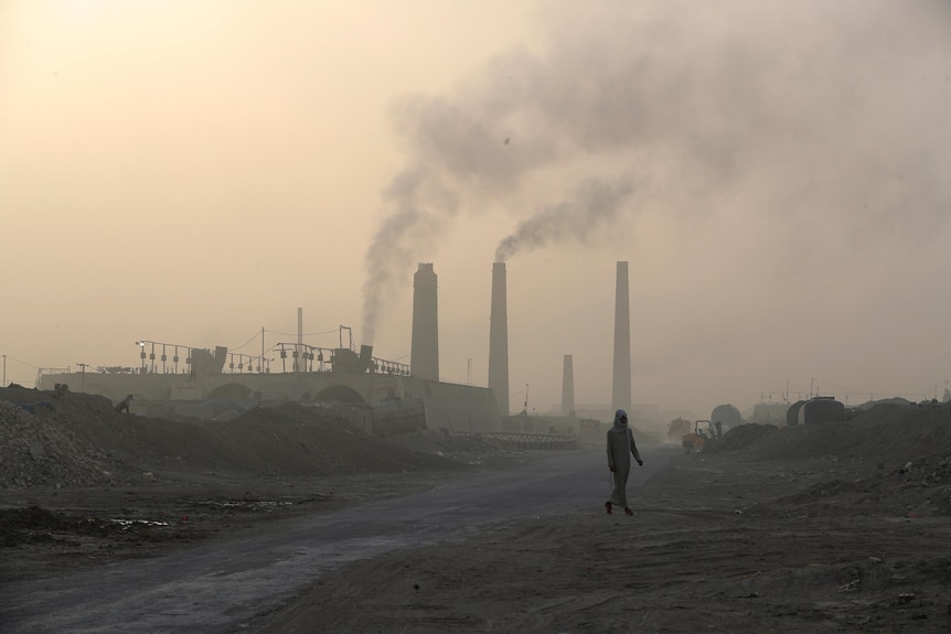 Scene of a smoggy area with a single person walking in the foreground and a dirty coal plant in background