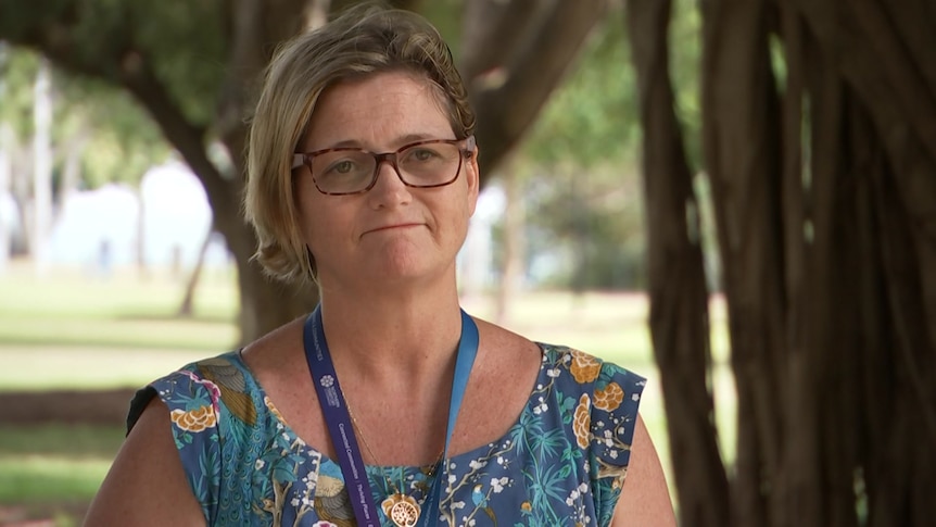 A woman with short hair and glasses in a sundress looks apologetic