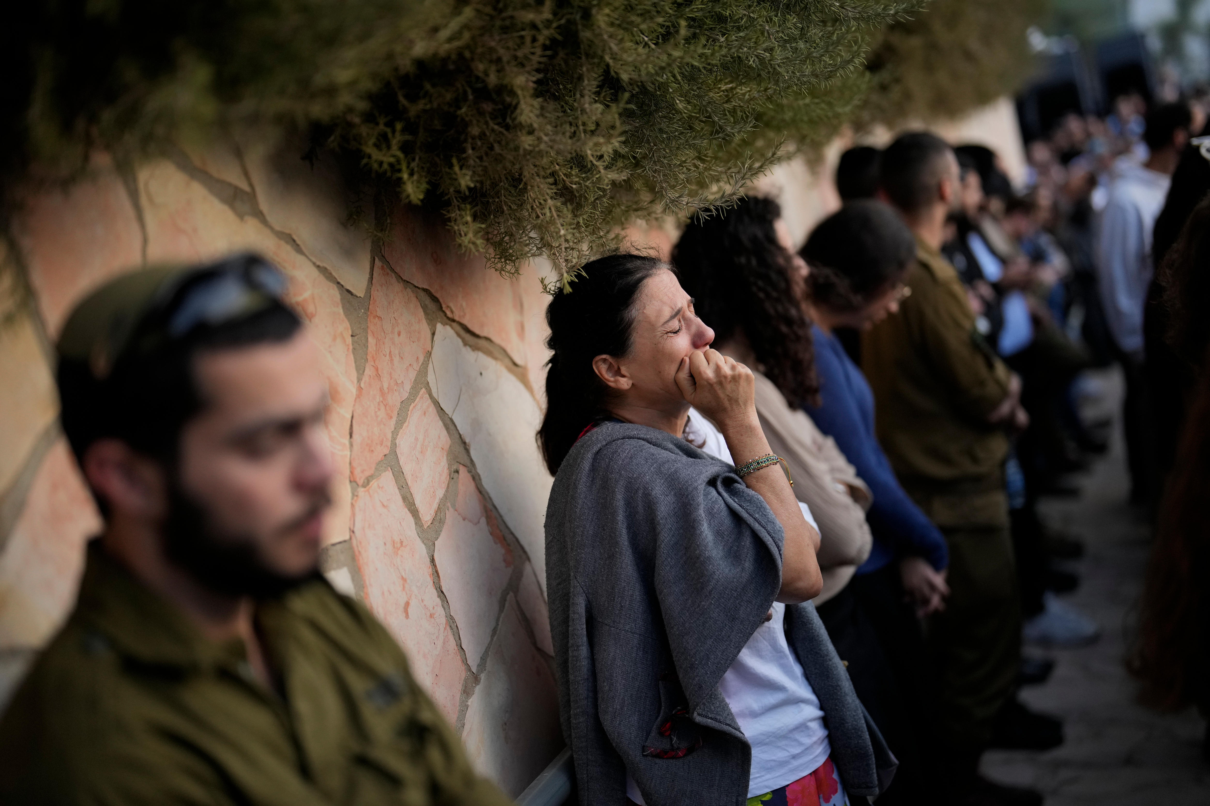 A woman sobs as people stand against a sandstone wall at a funeral