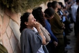 A woman sobs as people stand against a sandstone wall at a funeral