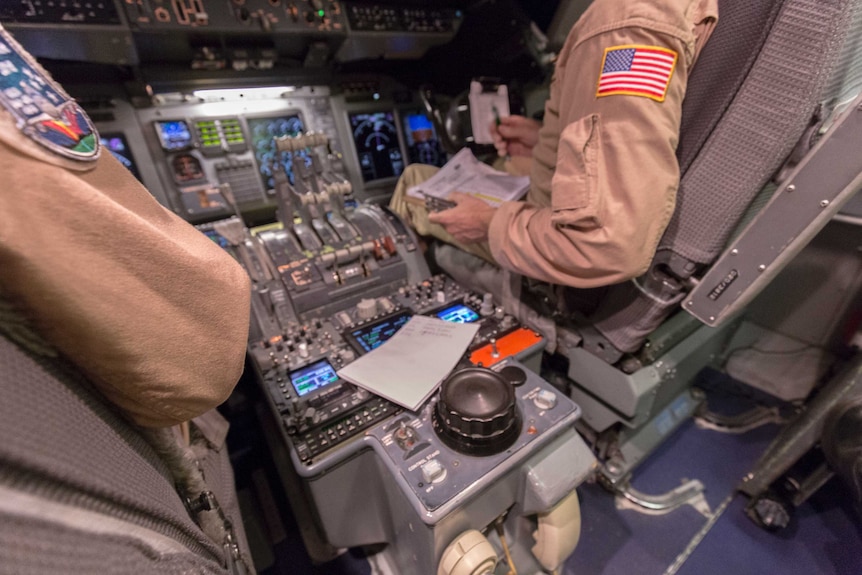 The central control panel of an 747, with pilots' arms bearing NASA insignia on their jumpsuits.