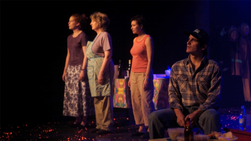 Four actors on a stage playing farmers and other members of a rural community, the stage floor is lit by embers