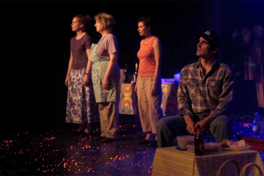 Four actors on a stage playing farmers and other members of a rural community, the stage floor is lit by embers