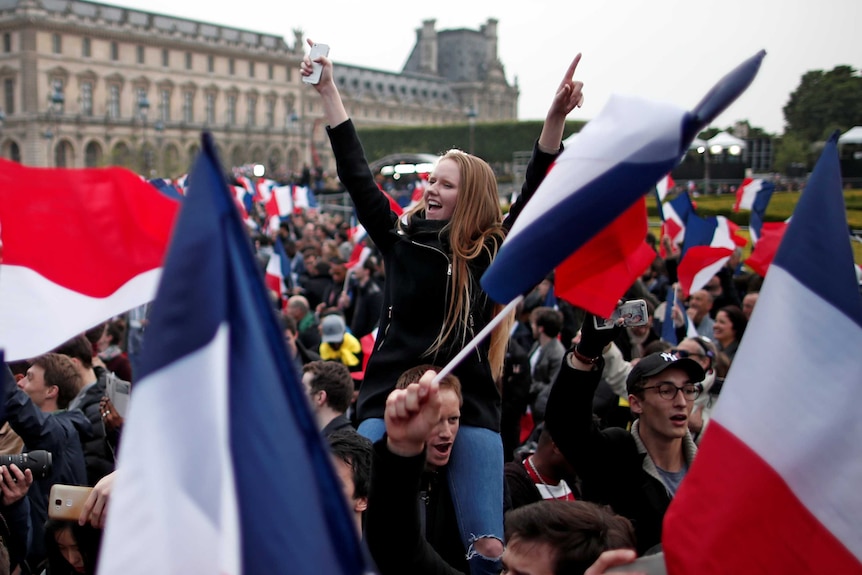 Supporters of Emmanuel Macron celebrate and wave flags near the Louvre museum after the French election results were announced.