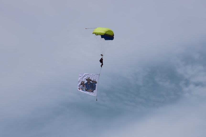 A flag with a picture of a man and two kids is carried by a paraglider.
