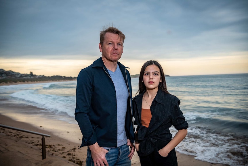 A teenager with her father on a beach at sunset