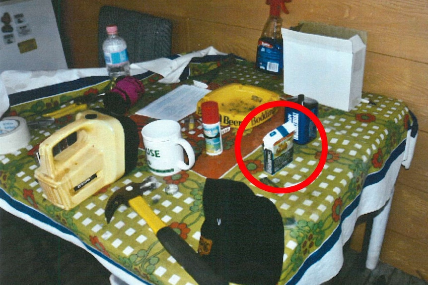 A kitchen table covered in a range of items including a cigarette packet, which is highlighted by a red circle.