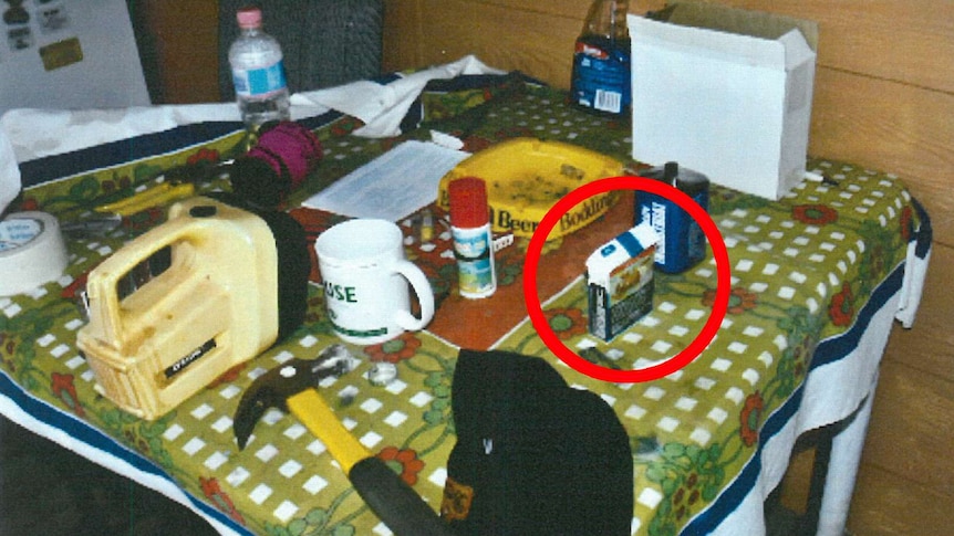 A kitchen table covered in a range of items including a cigarette packet, which is highlighted by a red circle.