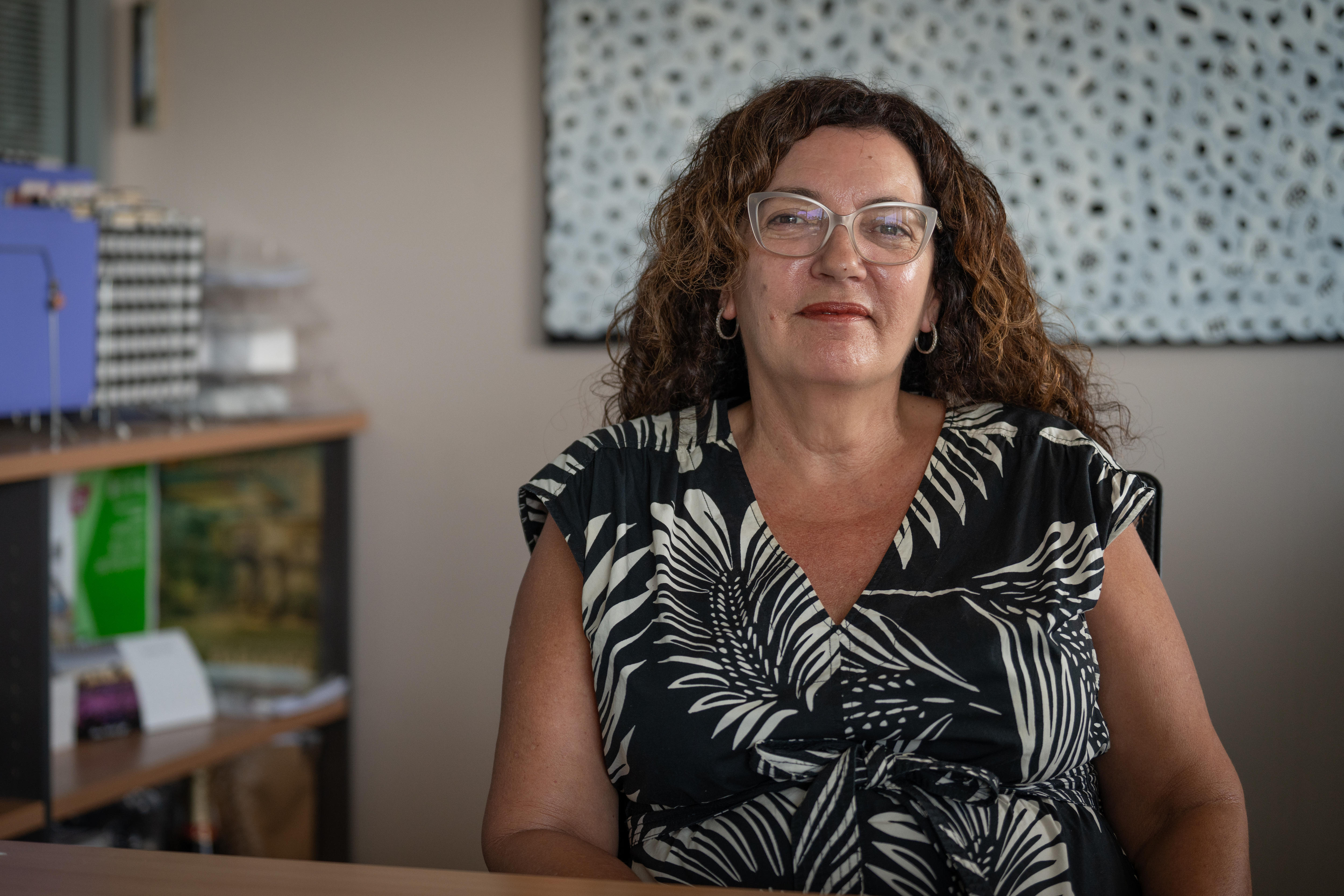A woman with curly hair, Kerri-Ann Laurence, sits in her office and smiles at the camera.
