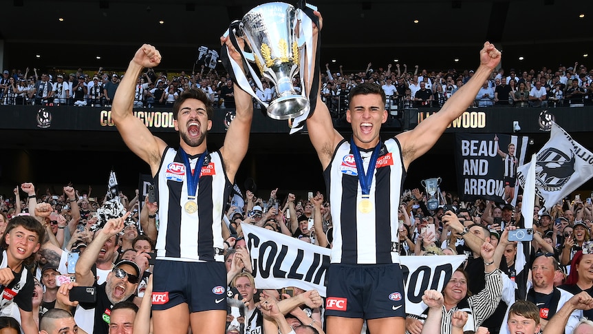 Josh and Nick Daicos hold aloft the AFL premiership trophy in front of Collingwood fans at the MCG.