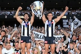 Josh and Nick Daicos hold aloft the AFL premiership trophy in front of Collingwood fans at the MCG.