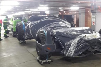 A Batmobile replica wrapped in plastic is parked in an underground carpark.