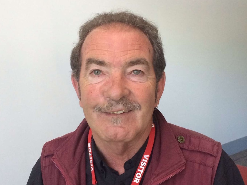 A man in a black shirt and red vest looks at the camera sitting down.